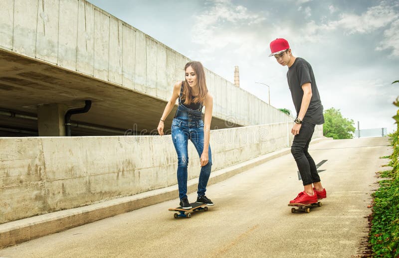 Skateboardfahrerfrau und -mann, welche unten die Steigung rollen