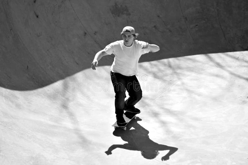 Black and white of a young skateboarder skating in the bottom of the bowl at a concrete skate park. Black and white of a young skateboarder skating in the bottom of the bowl at a concrete skate park.