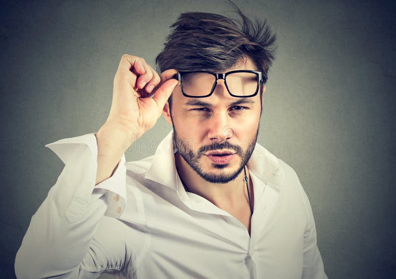 Young man in formal shirt taking off eyeglasses looking at camera with doubts. Young man in formal shirt taking off eyeglasses looking at camera with doubts.