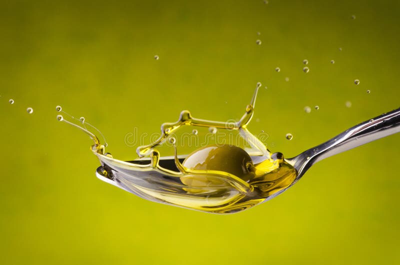 A spoon with oil splashing under a fall of green olive