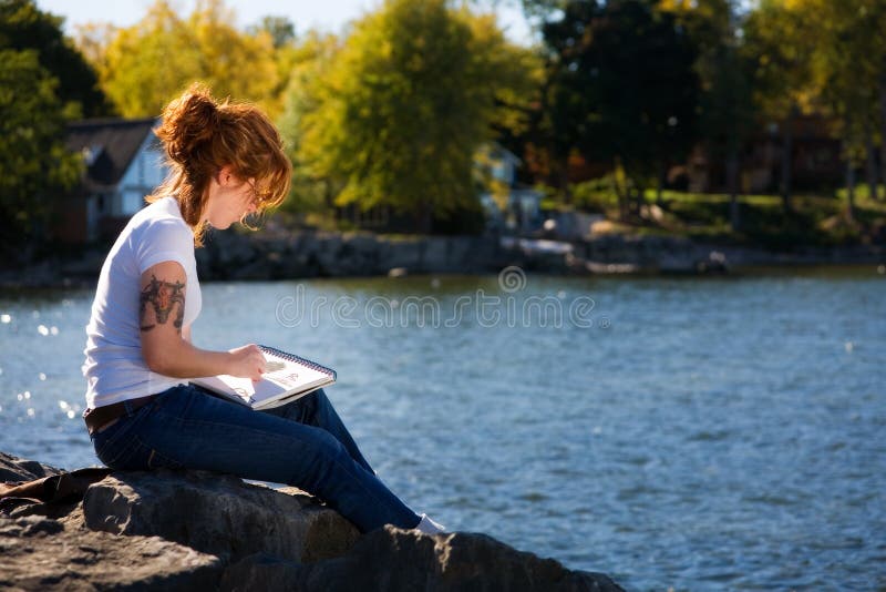Young woman sketching at a lakeshore. Young woman sketching at a lakeshore.