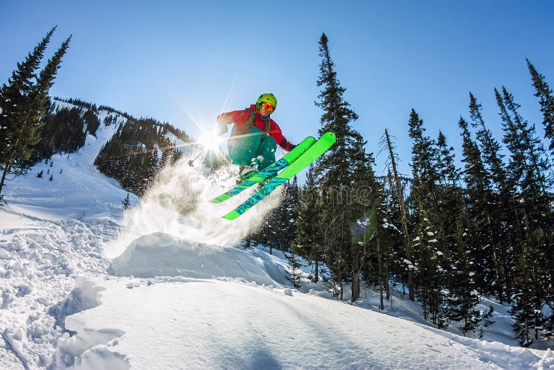 Skier freerider jumping from a snow ramp in the sun on a background of forest and mountains