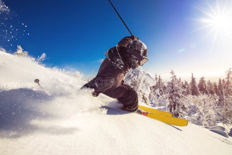 Skier skiing downhill during sunny day fresh snow freeride. Extreme High speed, frosty dust scatters.