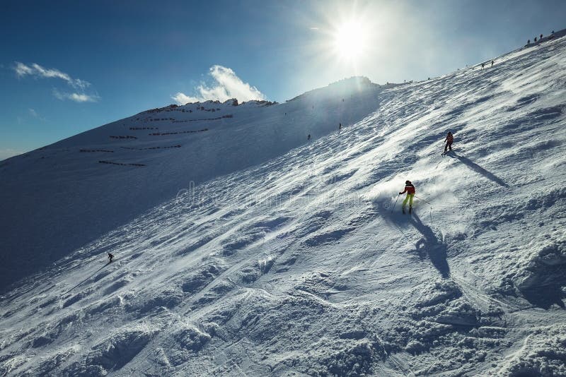 Lyžaři sjíždějí ze zasněženého horského kopce