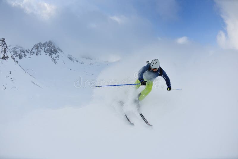 Skier skiing downhill on fresh powder snow with sun and mountains in background. Skier skiing downhill on fresh powder snow with sun and mountains in background