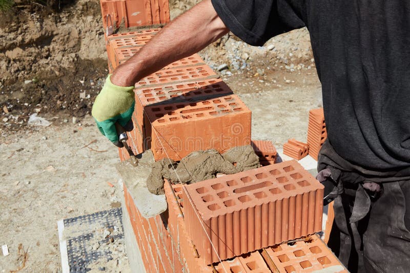 A skilled bricklayer is carefully applying mortar to red bricks, aligning them precisely to build a wall at a construction site royalty free stock photography