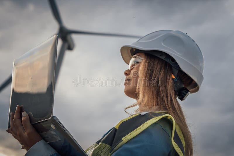A skilled female engineer uses her laptop to oversee complex wind turbine operations, showcasing her expertise and royalty free stock image