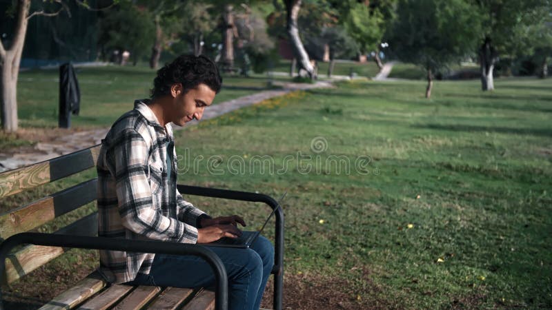 Skilled programmer Arabic man business freelancer working laptop sitting on bench at summer park stock footage