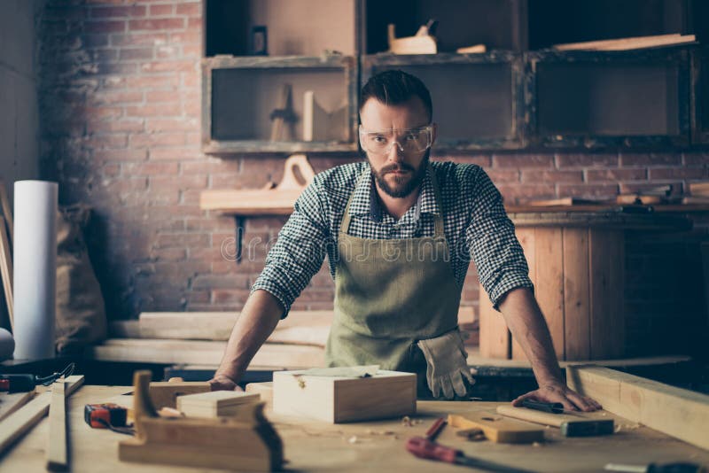 Skilled successful professional quolified pensive confident serious handsome bearded artisan dressed in work clothes is leaning o