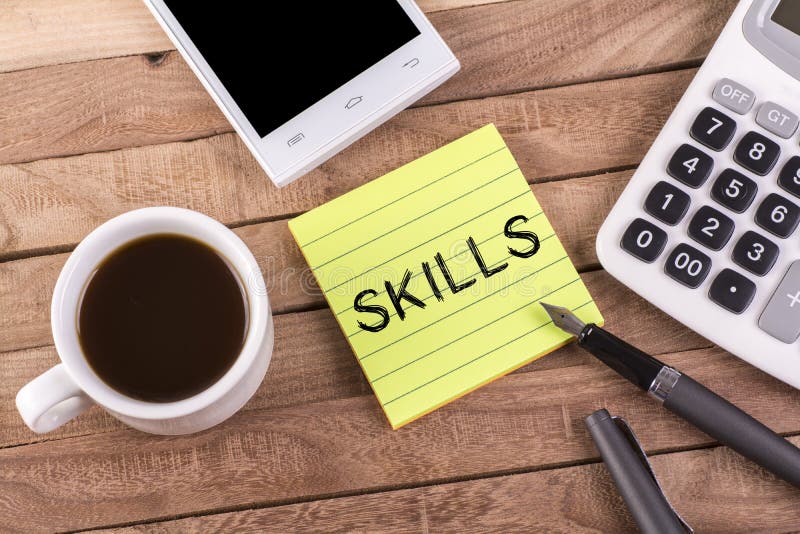 Skills word on memo with pen , coffee , mobile and calculator on wooden table