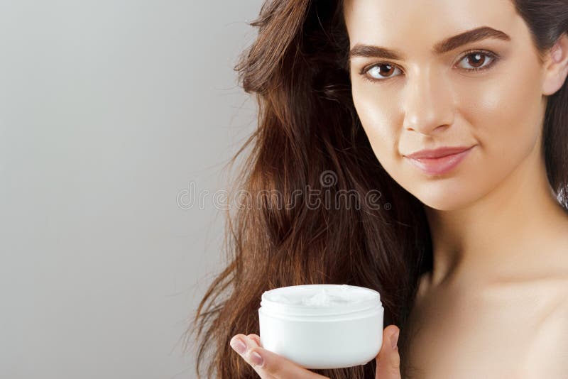 Skin care. Beauty Concept. Young pretty woman holding cosmetic cream. Soft skin and naked shoulders