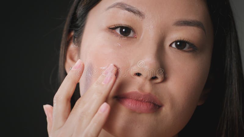 Skin moisturizing concept. Young asian woman applying nourishing cream on her under eye area, skin lifting procedures