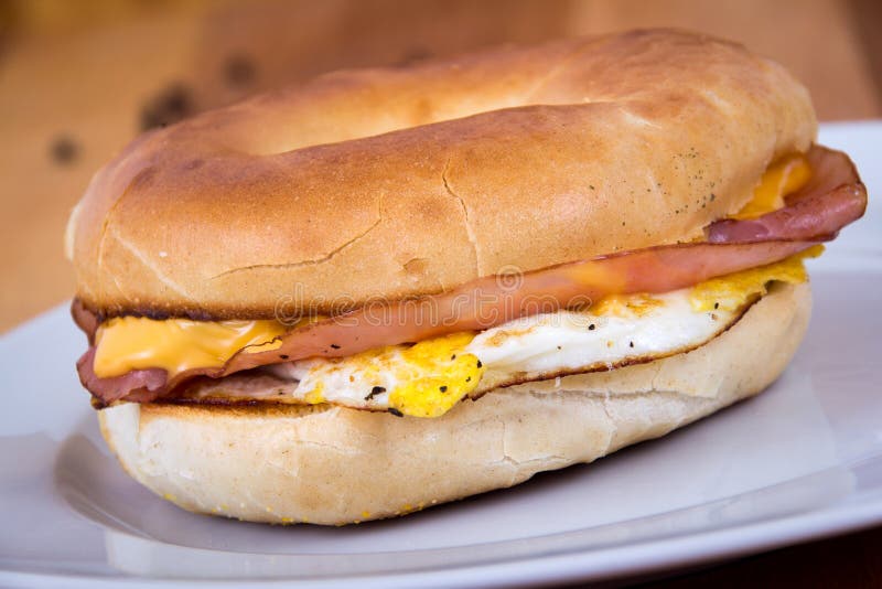 Skinka-, ägg- och ostfrukostsmörgås på en bagel royaltyfri foto Skinka-, ägg- och ostfrukostsmörgås på en bagel royaltyfri foto