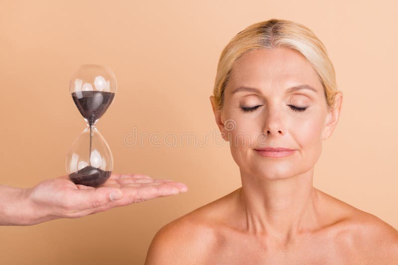 Skinnesdränkt lugn medelålders kvinna har skinkare spa salon procedur tid för att ändra isolerad beige färg bakgrund royaltyfri bild