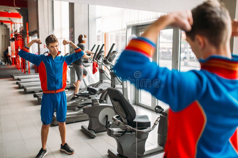 Skinny man watches on his muscles in mirror