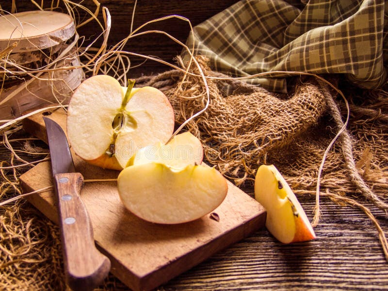 Skivat äpple på en lantlig bakgrund, med en kniv, en grön torkduk, ett hö och rep i bakgrunden