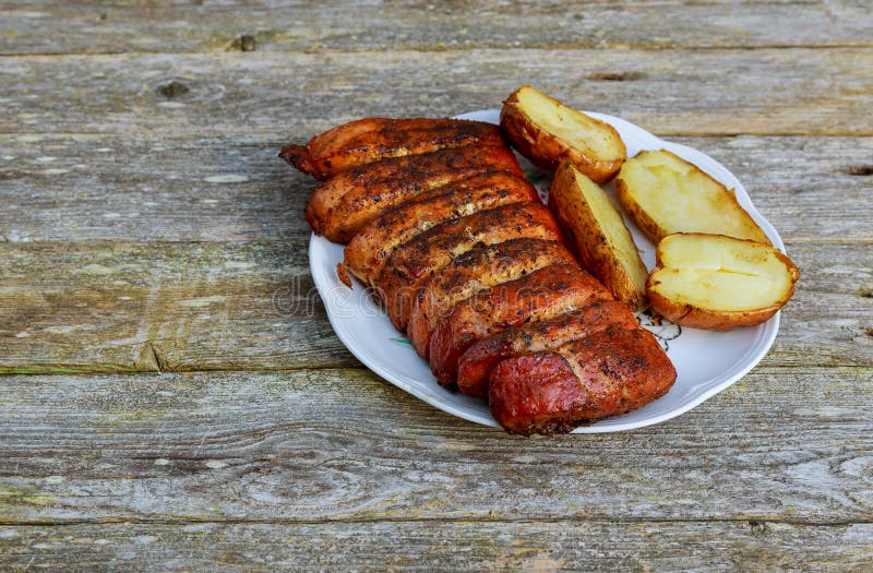 Skivor för grillfestgrisköttbiff på den vita plattan Grillade potatisar på den wood tabellen royaltyfri bild Skivor för grillfestgrisköttbiff på den vita plattan Grillade potatisar på den wood tabellen royaltyfri bild