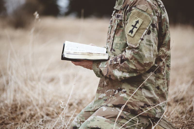 Skjutning av en ung soldat på knä medan en öppen bibel hålls på ett fält