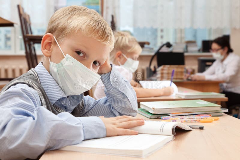 School children in medical face mask are learning in the half empty classroom during epidemic of flu. School children in medical face mask are learning in the half empty classroom during epidemic of flu.