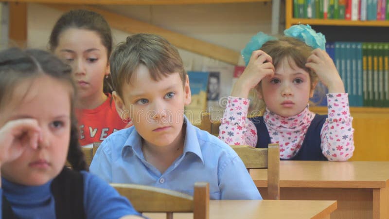 Skolbarn sitter på deras skrivbord och lyssnar till lärare