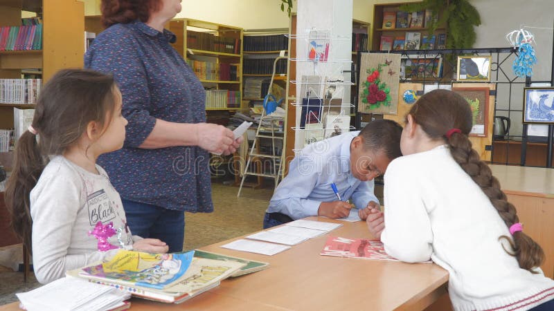 Skolbarn står bredvid lärarens skrivbord Den asiatiska skolpojken skriver på papper