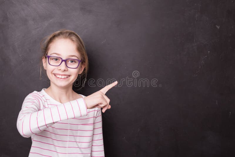 Skolbarnflickaunge, elev som pekar på svart tavla arkivbilder Skolbarnflickaunge, elev som pekar på svart tavla arkivbilder