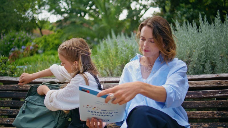 Skolflicka i skolan som tar med sig en bok som ger en kvinna i en ljuspark. Att göra läxor arkivfilmer