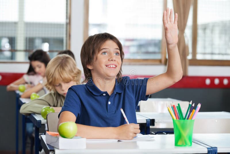 Skolpojke som lyfter handen, medan sitta på skrivbordet