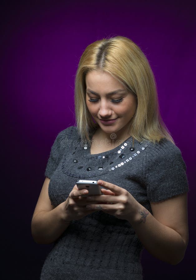 Skoncentrowanej blondynki mienia z włosami wzorcowy smartphone na czarnym tle zdjęcie stock Skoncentrowanej blondynki mienia z włosami wzorcowy smartphone na czarnym tle zdjęcie stock