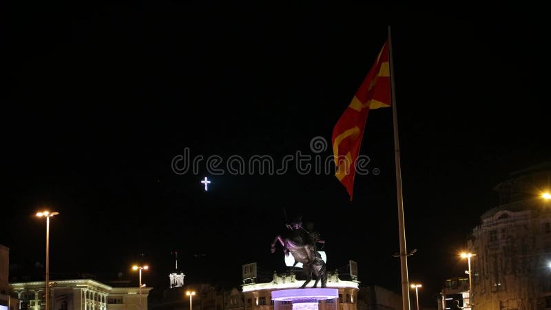 SKOPJE MACEDONIA - JULIO DE 2015: Alexander la gran estatua, la bandera macedónica y la cruz grande