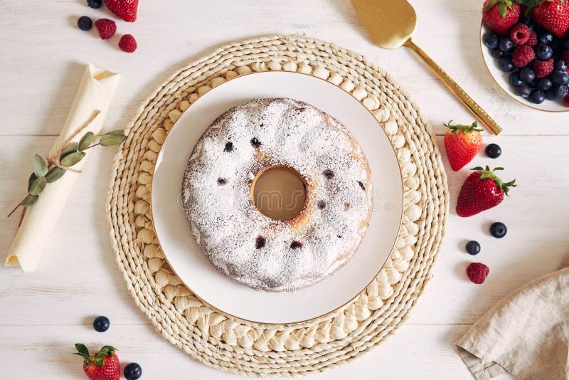 An overhead shot of a ring cake with fruits and powder on a white table with white background. An overhead shot of a ring cake with fruits and powder on a white table with white background