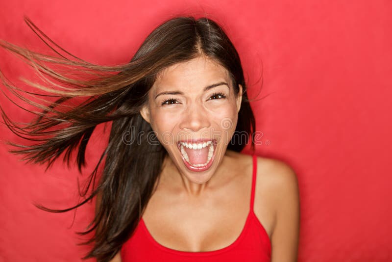 Scream. Woman screaming wild and crazy at full energy looking at camera on red background. Beautiful mixed race Asian Caucasian brunette female model with wind in the hair. Scream. Woman screaming wild and crazy at full energy looking at camera on red background. Beautiful mixed race Asian Caucasian brunette female model with wind in the hair.