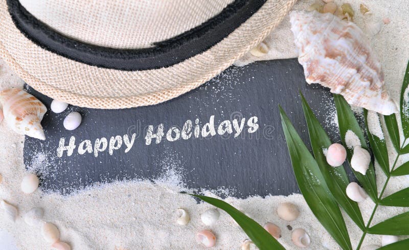 Happy holidays written on a slate in the sand with seashells and hat. Happy holidays written on a slate in the sand with seashells and hat