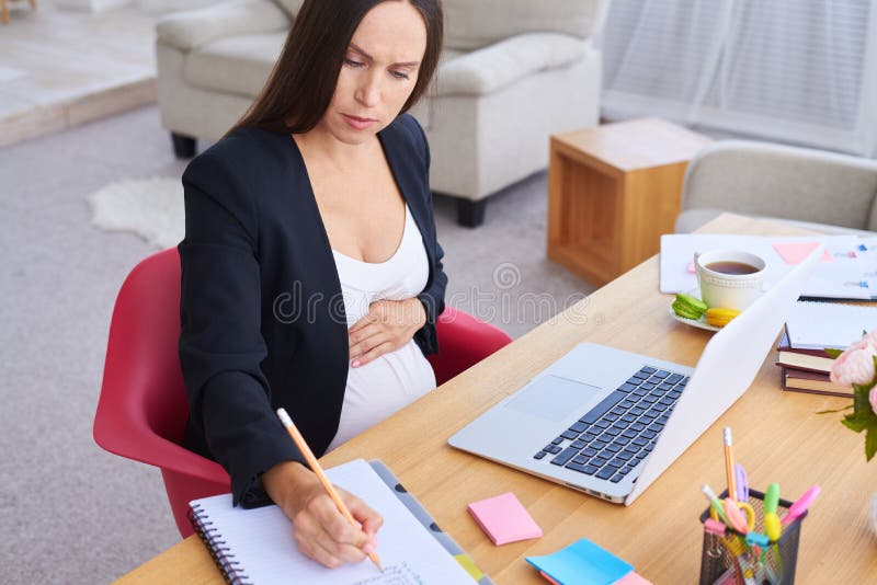 Skupiająca się ciężarna bizneswomanu mienia ręka na brzuchu podczas pracy obraz royalty free Skupiająca się ciężarna bizneswomanu mienia ręka na brzuchu podczas pracy obraz royalty free