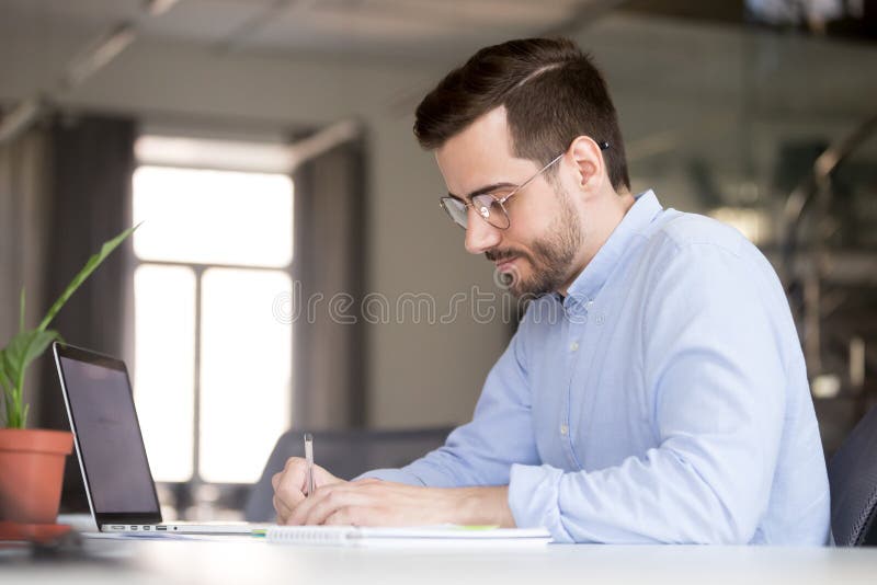 Focused business man making notes planning marketing economic research work with laptop, serious male student or worker writing studying online learning course preparing for test exam with computer. Focused business man making notes planning marketing economic research work with laptop, serious male student or worker writing studying online learning course preparing for test exam with computer