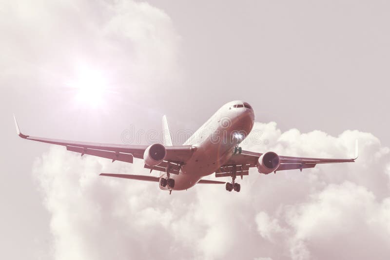 Sky with clouds and sun with a warm shade, reflected glare light, big passenger airplane landing approach airport