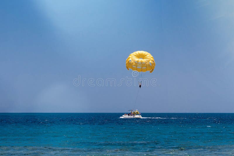 Skydiver Flying with a Yellow Parachute by Speed Boat on Sea. Skydiver