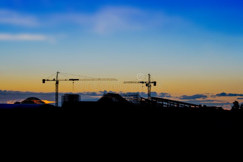 Skyline e silhueta do guindaste no local da construção civil no fundo da noite imagens de stock Skyline e silhueta do guindaste no local da construção civil no fundo da noite imagens de stock