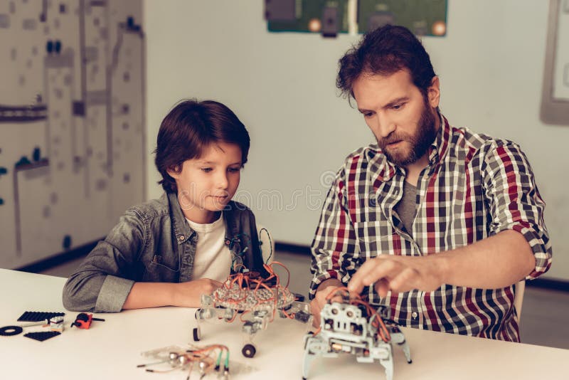 Skäggig fader och son som hemma konstruerar roboten royaltyfri fotografi Skäggig fader och son som hemma konstruerar roboten royaltyfri fotografi