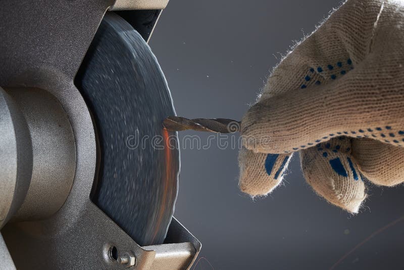 Horizontal shot of sharpening drill. The hand wearing a work glove of man regrinding the drill tool for sharpen the drill tool with grinding wheel. Horizontal shot of sharpening drill. The hand wearing a work glove of man regrinding the drill tool for sharpen the drill tool with grinding wheel.