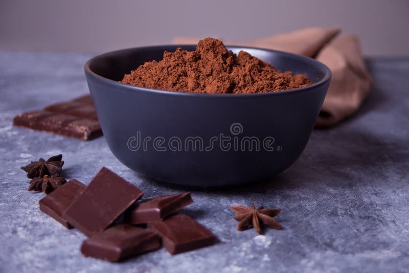 Skål med kakaopulver och chokladbitar på grå botten arkivbilder Skål med kakaopulver och chokladbitar på grå botten arkivbilder