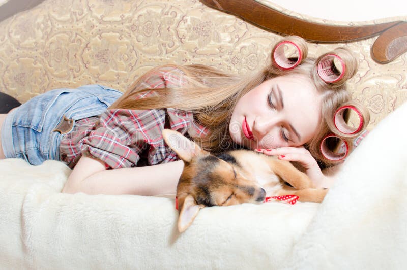 Slaapschoonheden: leuk hond en blonde mooi pinupmeisje met rode lippenkrulspelden in haar haar die in gesloten bedogen liggen stock foto's Slaapschoonheden: leuk hond en blonde mooi pinupmeisje met rode lippenkrulspelden in haar haar die in gesloten bedogen liggen stock foto's