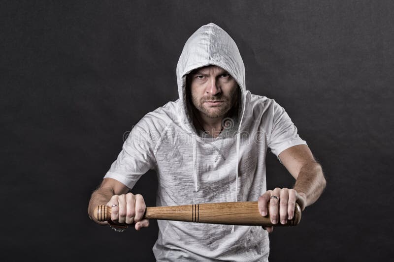 Slagträ för huliganhållbaseball Skäggig huv för mankläder i hoodietshirt Gangstergrabben hotar med slagträvapnet Agression eller royaltyfri bild Slagträ för huliganhållbaseball Skäggig huv för mankläder i hoodietshirt Gangstergrabben hotar med slagträvapnet Agression eller royaltyfri bild