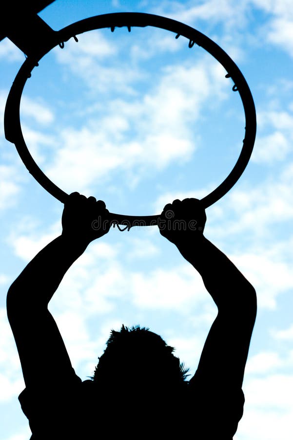 Silhouette of a Young Man hanging on to a basketball hoop. Silhouette of a Young Man hanging on to a basketball hoop