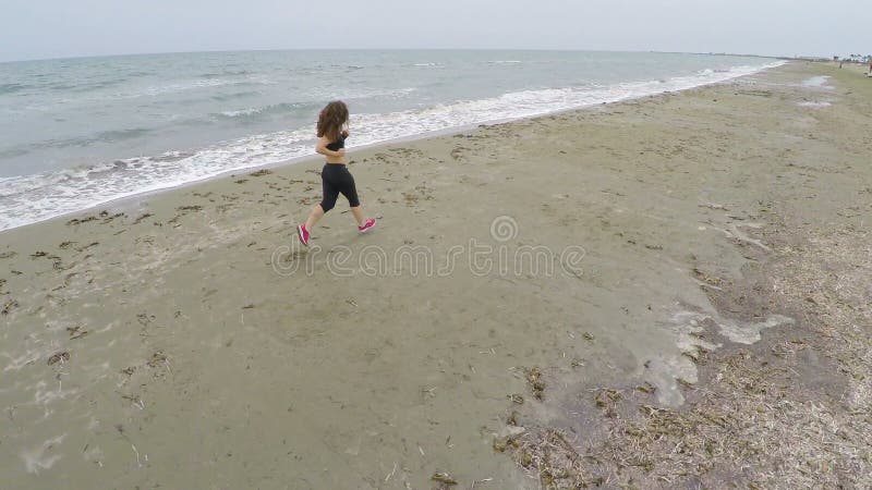 Slanke vrouw die langs leeg strand lopen, en van mening, luchtschot opleiden genieten