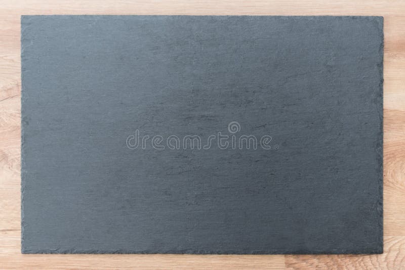 Slate board on wooden background. Black and gray slate textured flat stone laying on brown wooden desk table background