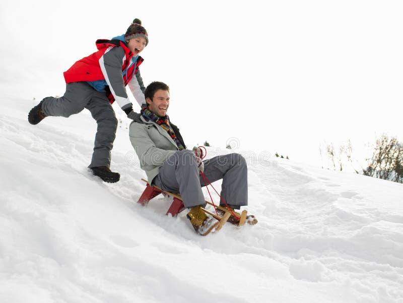 Young Father And Son Sledding down a hill having fun. Young Father And Son Sledding down a hill having fun