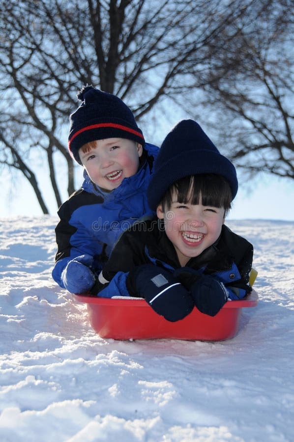 Two little boys have fun together sliding downhill on a pleasant winter day. Two little boys have fun together sliding downhill on a pleasant winter day.