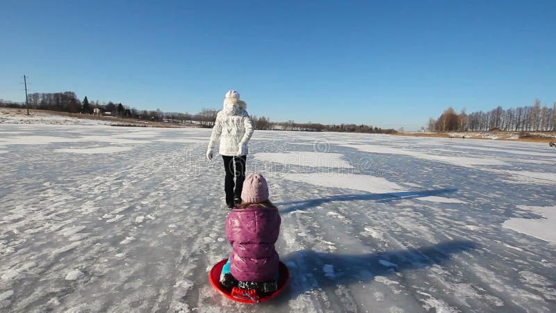 Sledding αδελφή κοριτσιών στην παγωμένη λίμνη