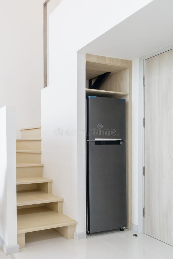Sleek refrigerator fitted under a staircase, maximizing space in a minimalist, modern home. This design showcases smart use of under-stair storage and efficient appliance placement. Sparse use stock images, royalty-free photos and pictures